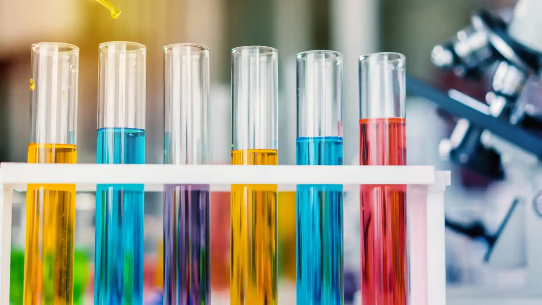 Éprouvettes multicolores sur un support acrylique blanc avec un microscope en arrière-plan