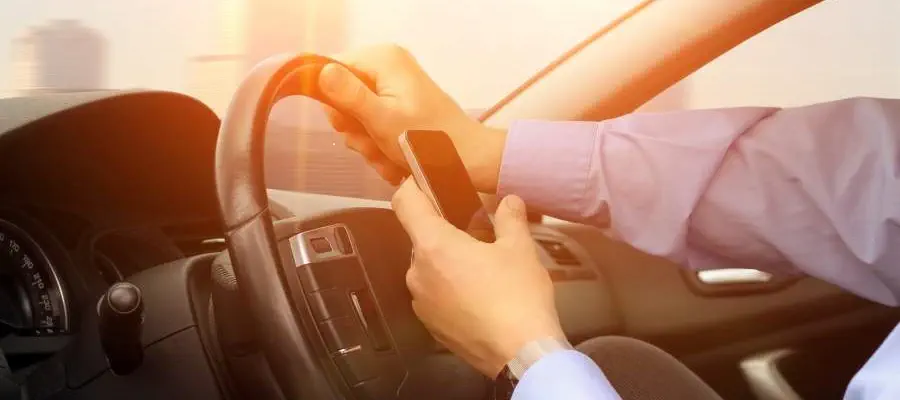 Conducteur au volant de la main droite téléphonant sur son smartphone de la main gauche